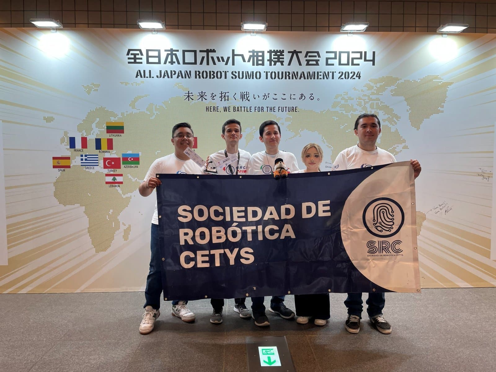 Integrantes de la Sociedad de Robótica CETYS con el estandarte SRC frente al muro oficial del All Japan Robot-Sumo Tournament 2024 en Tokio